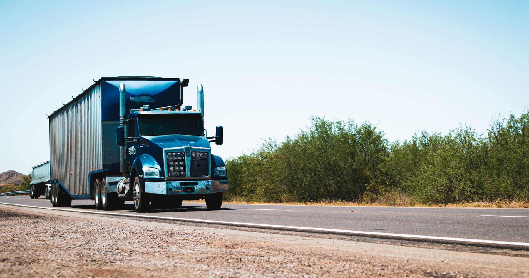 Blue 18-wheeler tractor-trailer on a wide, flat Texas interstate under a clear sky near Fort Worth