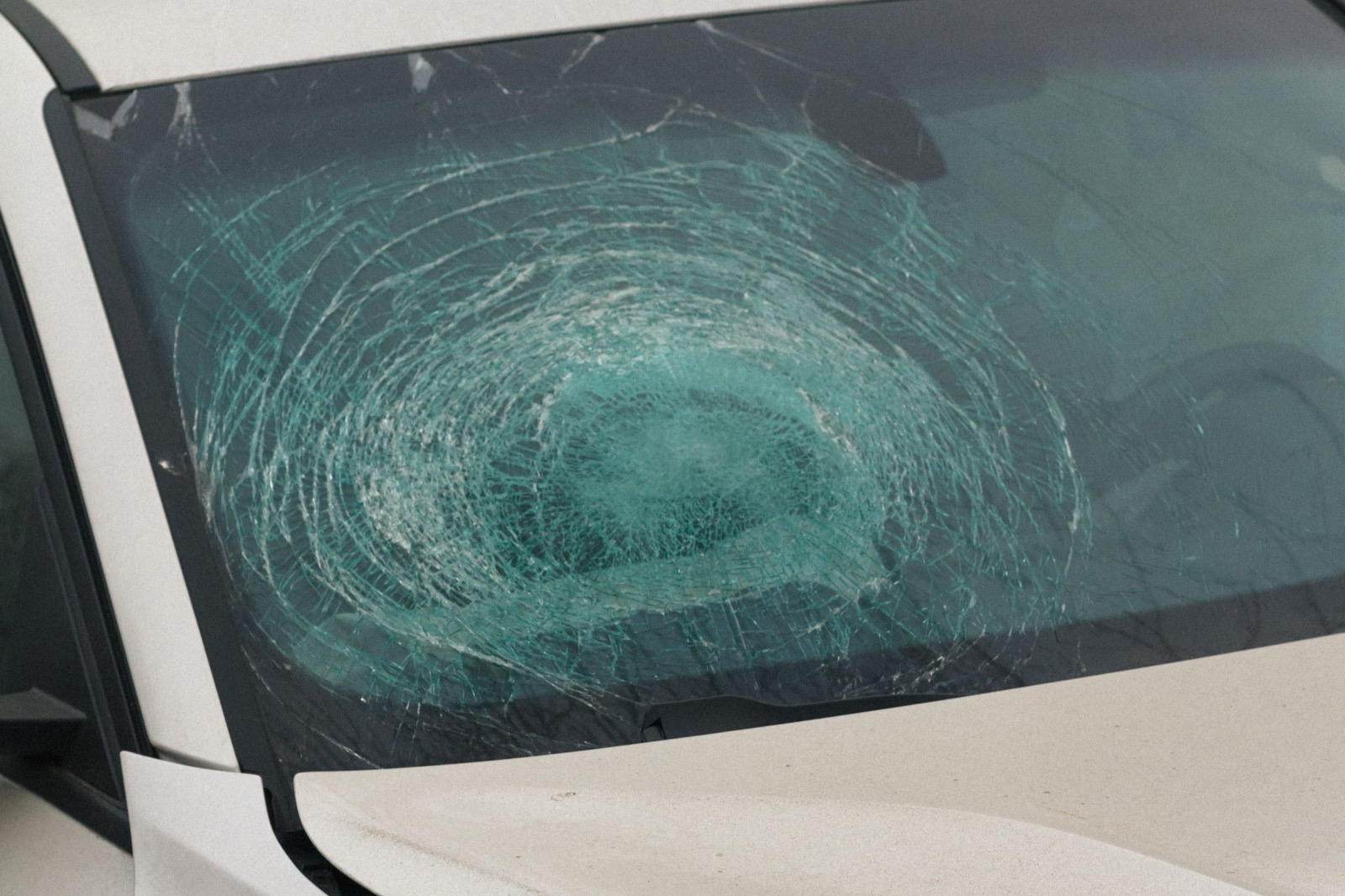 Spidered windshield and crumpled hood of a white car after a collision