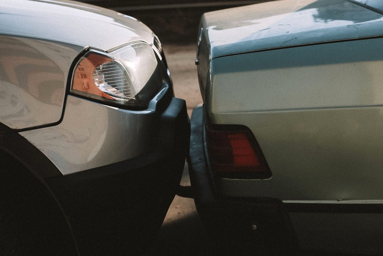 Front bumper of a silver car pressed against the rear bumper of a light blue sedan after a low-speed rear-end collision