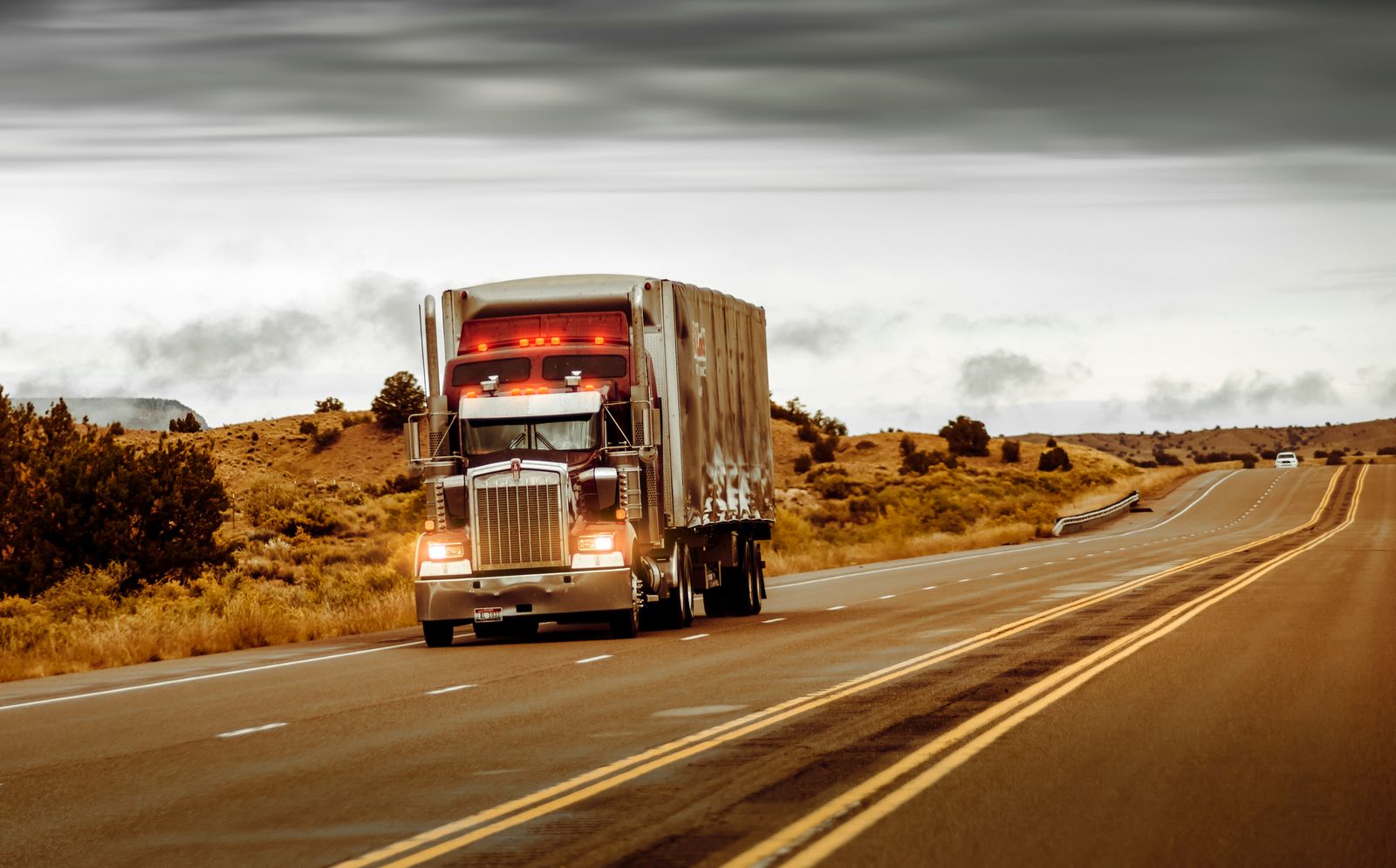 18-wheeler headed down a divided desert highway under a stormy sky