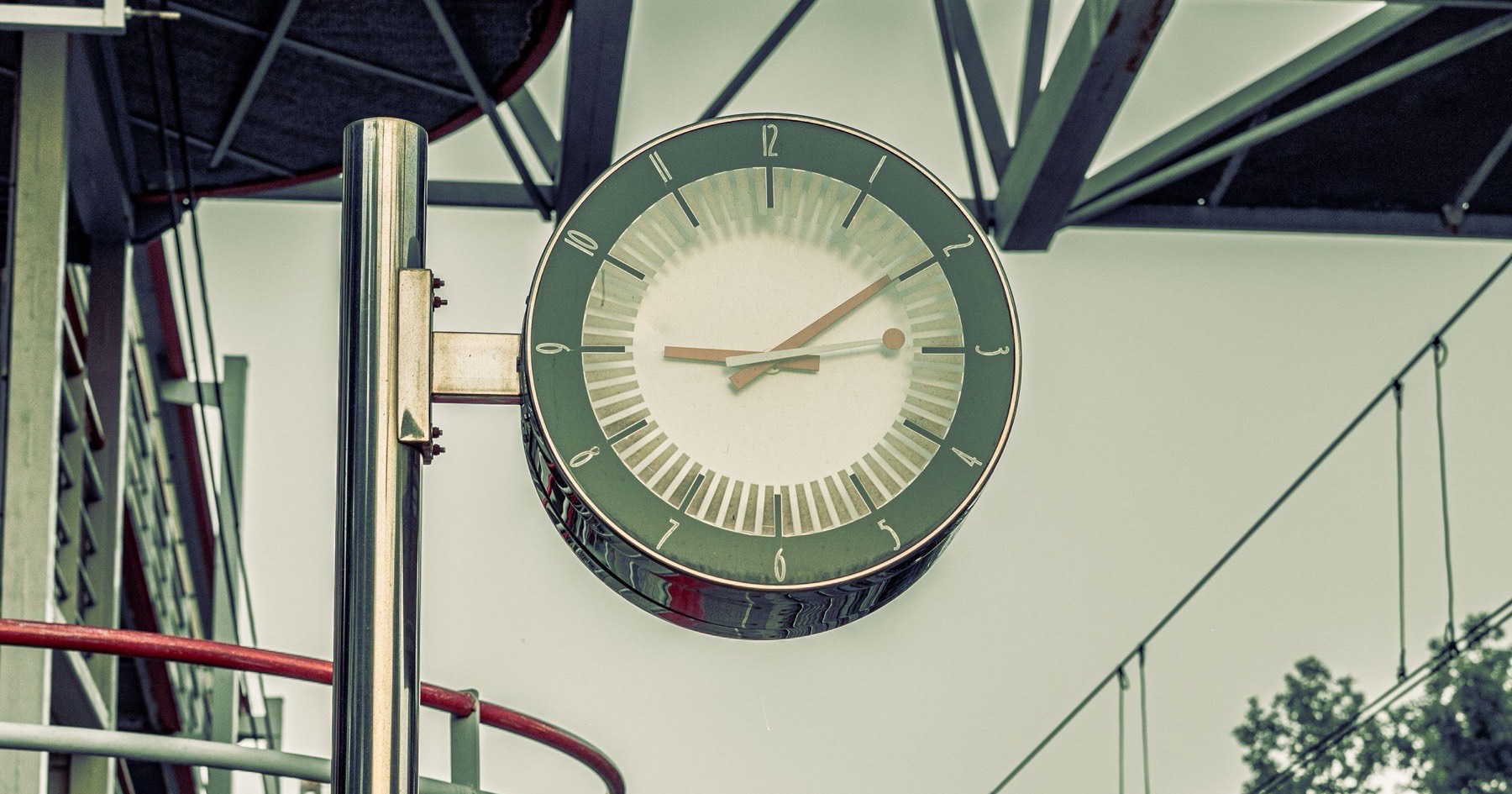 Large analog clock mounted on a pole over an empty rail platform under an overcast sky