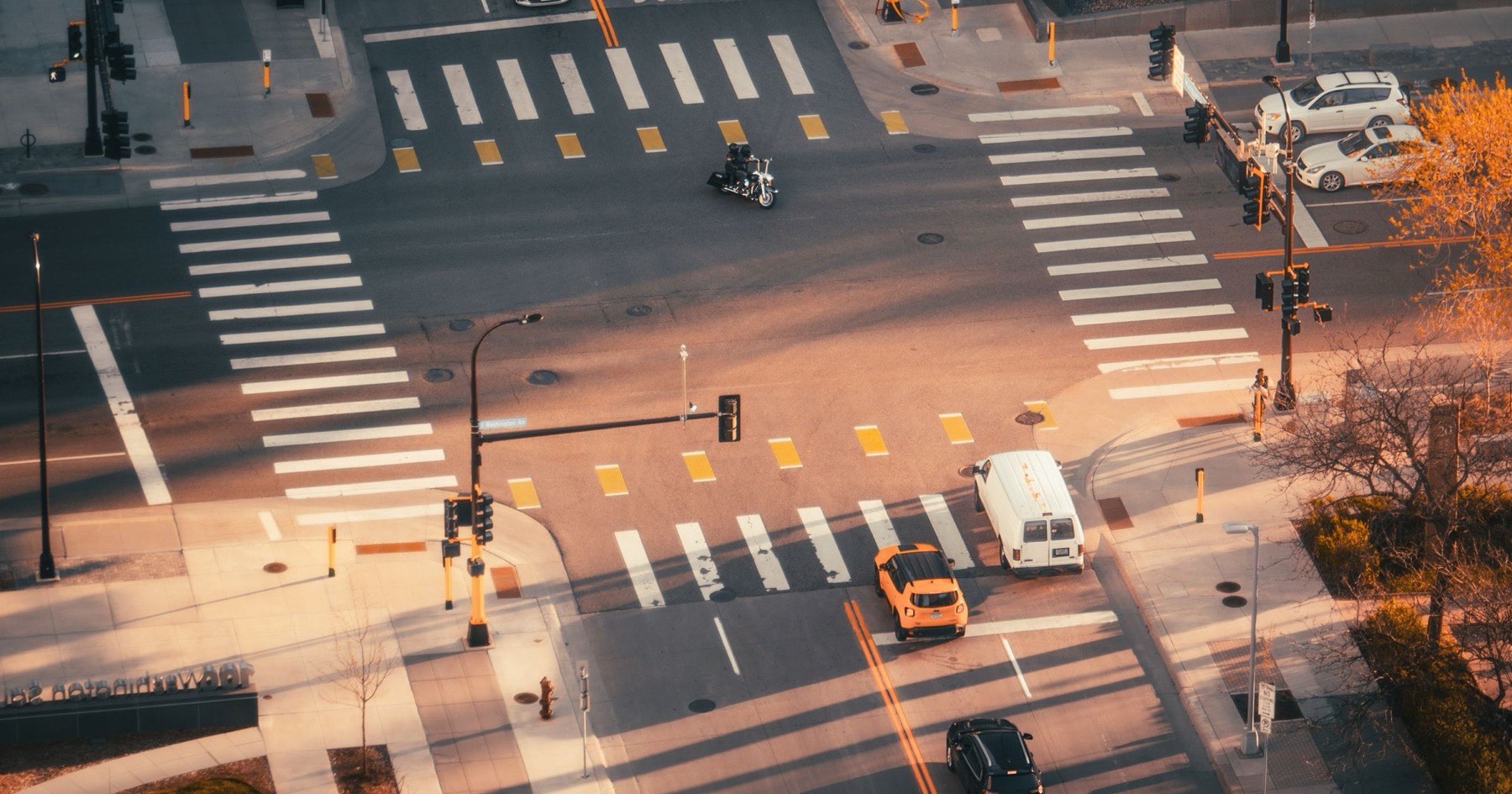 Aerial view of a downtown intersection with crosswalks, a van and cars crossing at golden hour