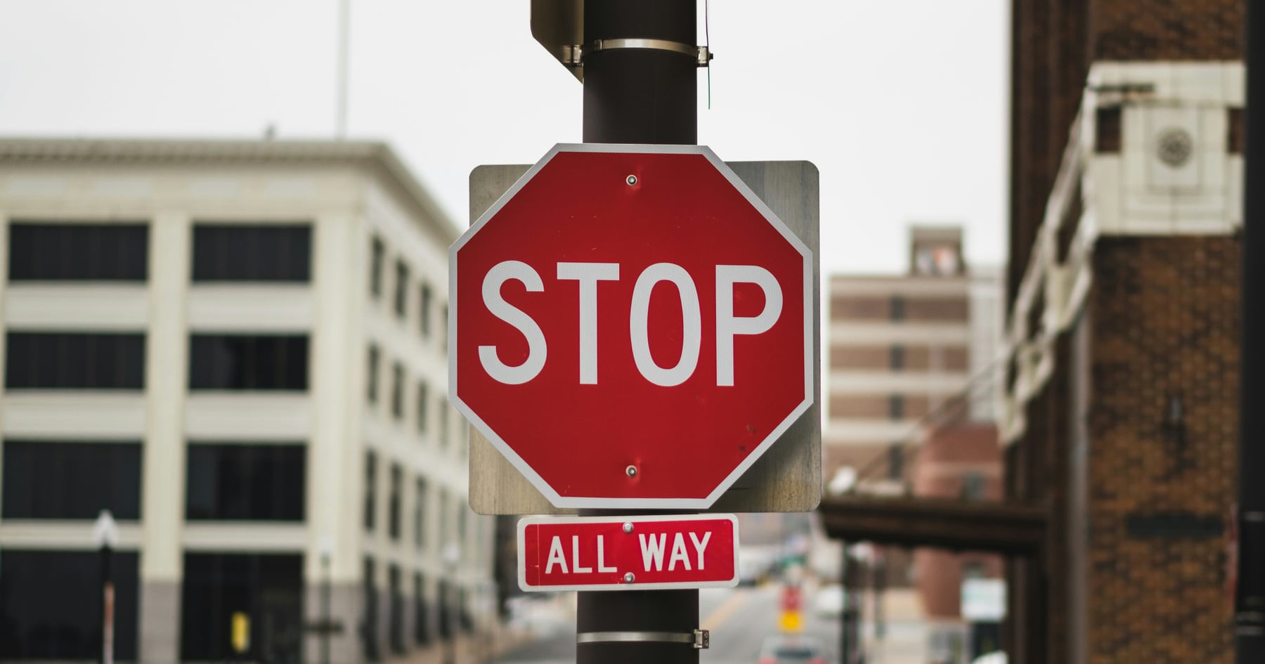 Red stop sign with an All Way plate on a downtown street corner