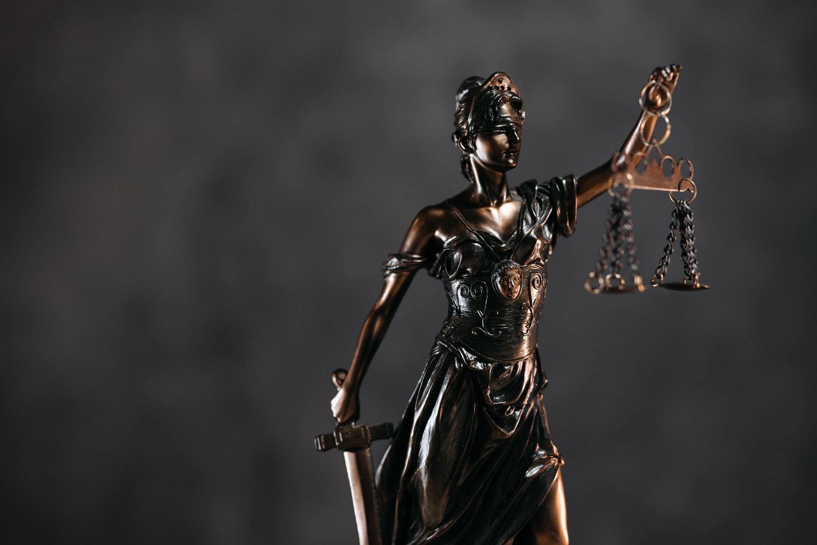 Bronze Lady Justice statue holding balanced scales against a dark background
